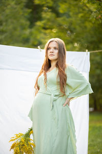 Pregnant woman with big belly, yellow goldenrod solidago flowers in hands. white female wears dress