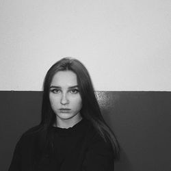 Portrait of young woman standing against wall