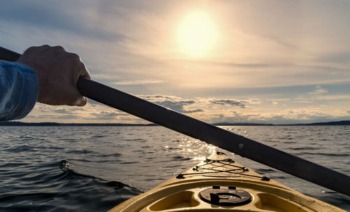 Cropped image of hand kayaking on sea against sky during sunset