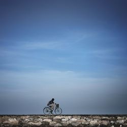 Woman riding bicycle on field against sky