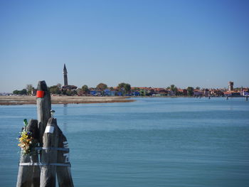 Rear view of man looking at sea by buildings against clear sky