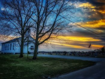 Bare tree on landscape against sky at sunset