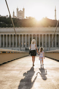 Rear view of mother with daughter walking on palais-de-justice footbridge against sky during sunset