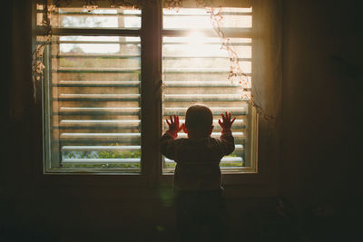 A baby looking through a window covered with lace curtain in sunset