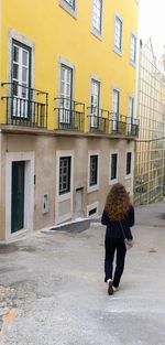 Rear view of woman walking on street by buildings