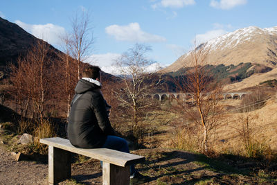 Man sitting on bare tree against sky