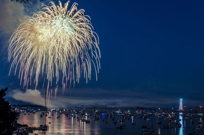 Firework display over sea against sky at night