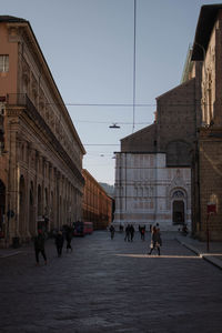 People walking on street amidst buildings in city against sky