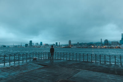 Rear view of man standing on railing against buildings in city