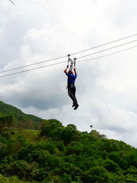 Low angle view of men paragliding hanging against sky