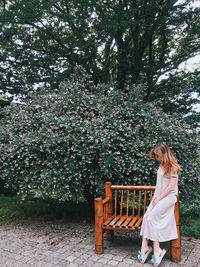 Side view of woman sitting in bench against plants