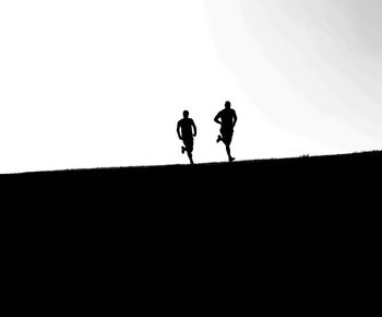 Silhouette men running on field against sky