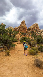 Hiker walking towards rock formations against sky
