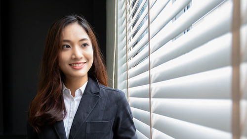 Portrait of young woman standing against window