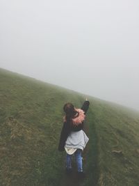 Rear view of girl standing on grassy landscape against sky during foggy weather