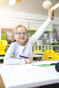 Girl with hand raised sitting at desk in classroom