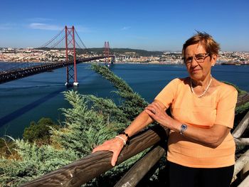 Portrait of woman standing with april 25th bridge over tagus river in background