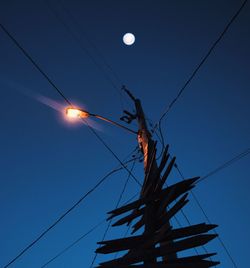 Low angle view of power lines and illuminated street light against blue sky