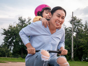 Happy friends sitting on woman holding umbrella against trees