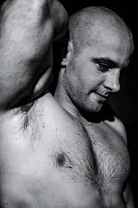 Close-up of shirtless man looking away against black background