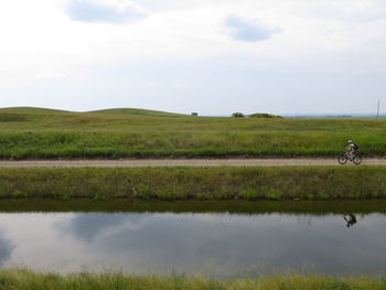 Scenic view of grassy field by lake against sky