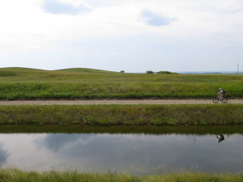 Scenic view of grassy field by lake against sky