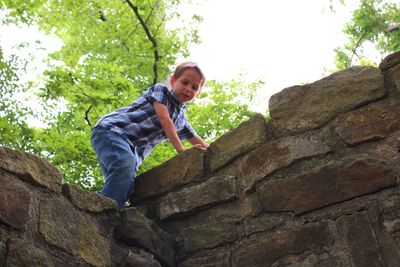 Portrait of happy boy standing on rock against sky