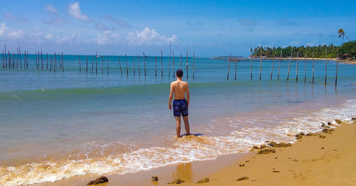 Rear view of shirtless man standing at beach against sky