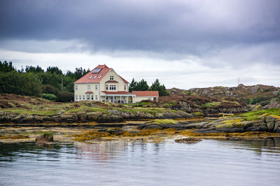 House by lake and buildings against sky