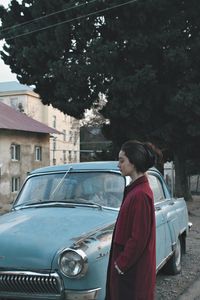 Young woman standing by car against trees