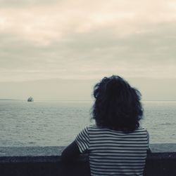 Rear view of woman standing on beach against sky