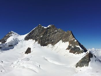 Low angle view of snowcapped mountain against clear blue sky