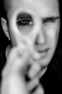 Portrait of young man looking through metal held by friend against black background