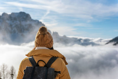 Rear view of female hiker wearing winter clothes looking at amazing view of mountains