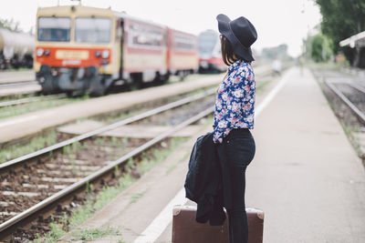 Side view of woman with suitcase waiting while standing on railroad station
