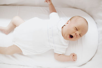 Newborn baby yawning in the crib with close eyes and open mouth