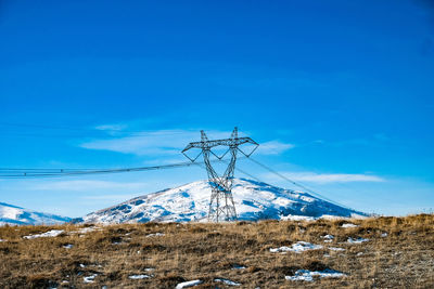 Electricity pylon on snowcapped mountain against blue sky