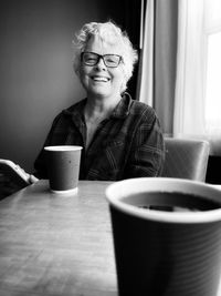 Mature woman using mobile phone and drinking coffee at home