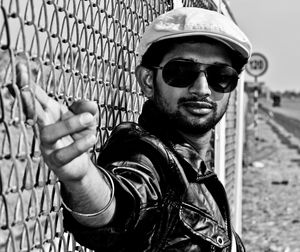 Portrait of young man by metal fence on field