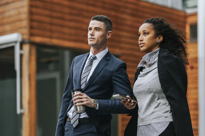 Male and female business professionals looking away while waiting at street