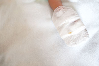 Cropped baby hand with bandage on bed