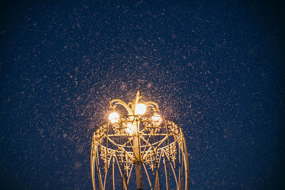 Illuminated electric lamp against sky at night