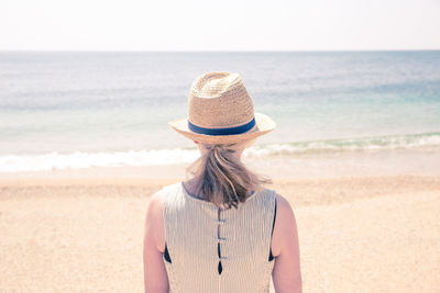 Rear view of mature woman wearing hat while standing at beach against clear sky during sunny day