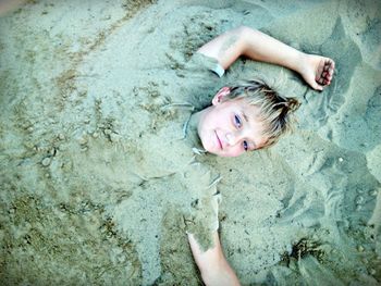High angle portrait of boy buried in sand at beach