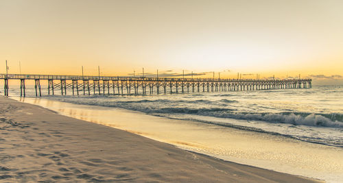 Pier on beach against clear sky during sunset