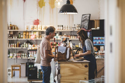 Side view of female sales clerk with customer at checkout counter in deli