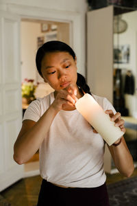 Young woman standing with lit candle at home