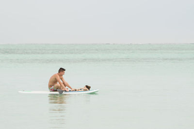 Friends paddleboarding in sea against sky