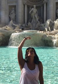 Smiling young woman gesturing against trevi fountain