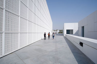 People walking on modern building against clear sky